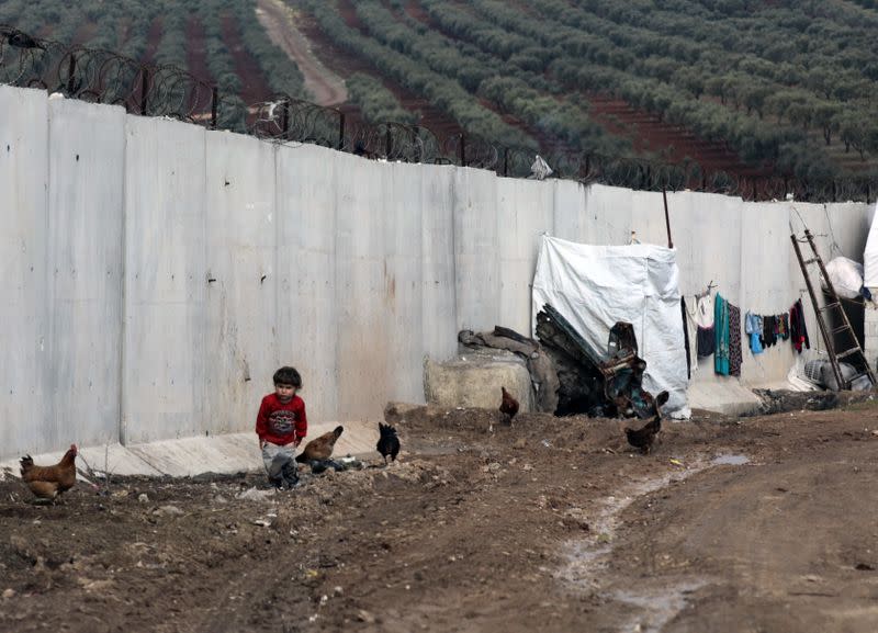 An Internally displaced child stands next to the wall in Atmah IDP camp, located near the border with Turkey