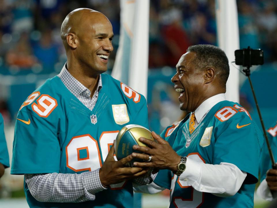 Jason Taylor (99) is presented a football by Nat Moore, another former Dolphins great, during the Dolphins All-Time 50th Anniversary Team ceremony at halftime of a game against the New York Giants, Monday, Dec. 14, 2015, in Miami Gardens, Fla.