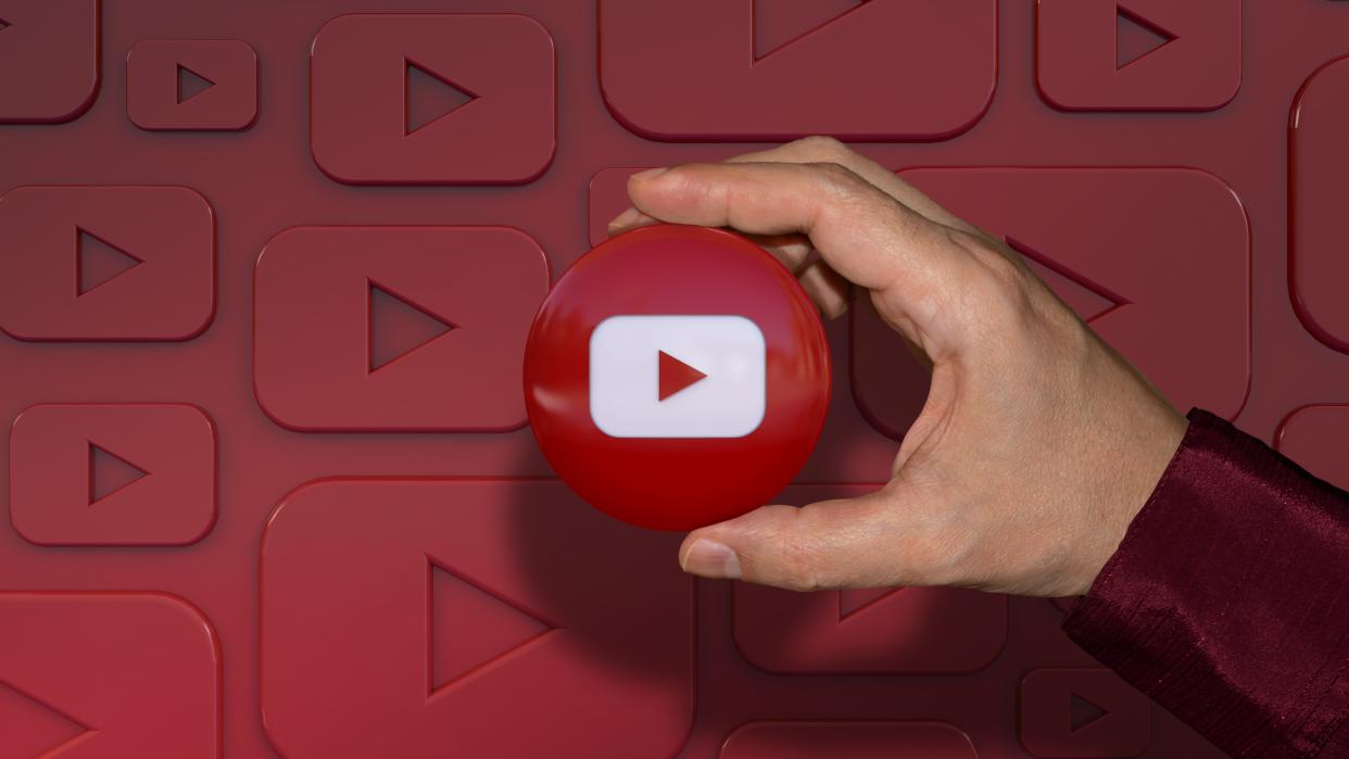  A hand holding a youtube logo glossy badge over dark red background. 