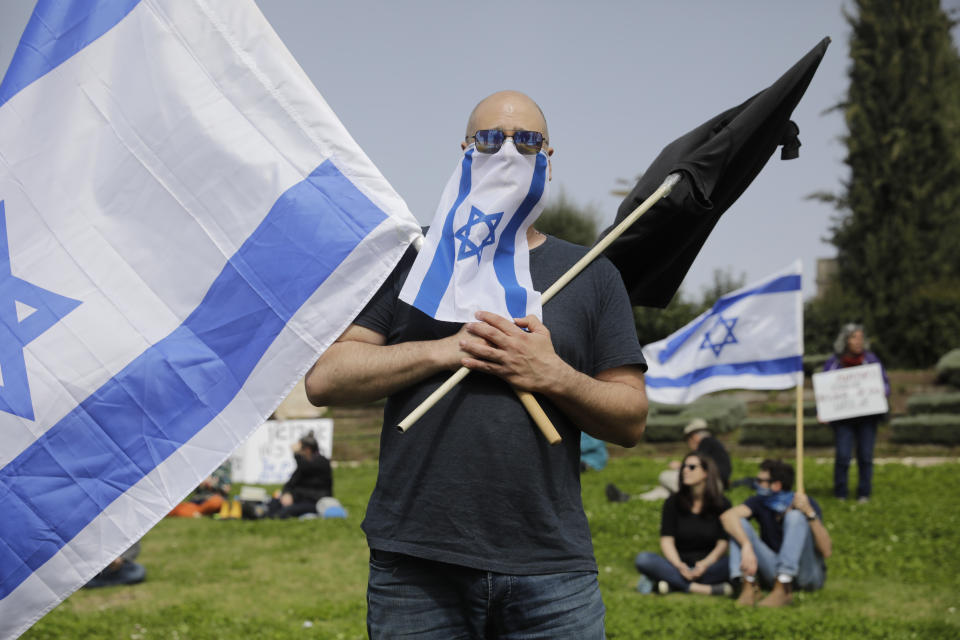 Israelis hold national flags during a protest against Prime Minister Benjamin Netanyahu outside the national parliament in Jerusalem, Monday, March 23, 2020. The opposition has accused Netanyahu of using the coronavirus crisis as cover to undermine the country's democratic institutions. With the country in near-shutdown mode, Netanyahu has already managed to postpone his own pending criminal trial and authorize unprecedented electronic surveillance of Israeli citizens. (AP Photo/Sebastian Scheiner)