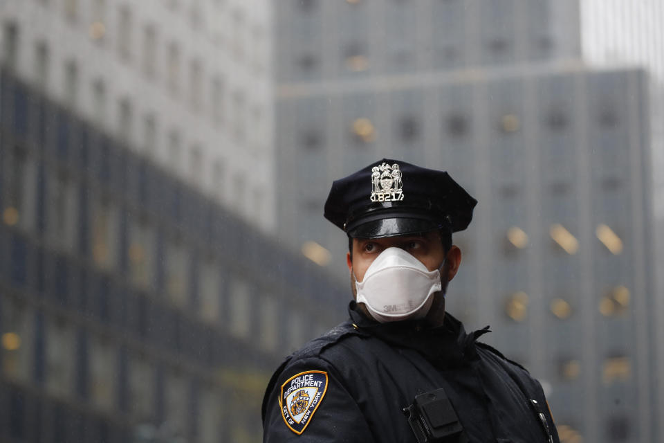 FILE - In this, May 1, 2020, file photo, a New York Police officer wears a mask to protect against coronavirus during a May Day protest outside the offices of New York Gov. Andrew Cuomo in New York. New York City Mayor Bill de Blasio and Gov. Andrew Cuomo are again at odds, this time over city police officers' eligibility for COVID-19 vaccines. (AP Photo/John Minchillo, File)