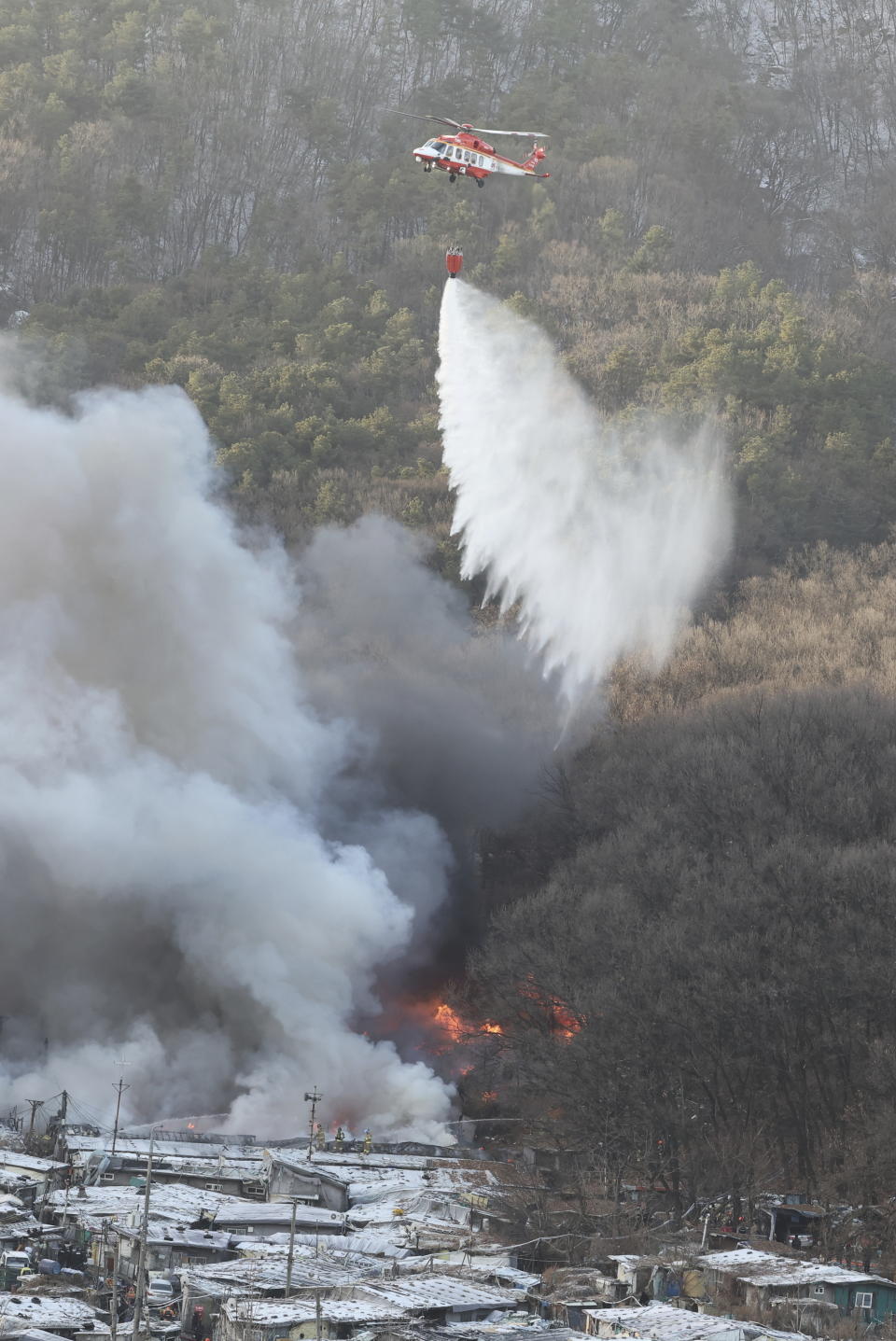 A National Fire Agency helicopter dumps water on a fire at Guryong village in Seoul, South Korea, Friday, Jan. 20, 2023. About 500 South Koreans were forced to flee their homes after a fire spread through a low-income neighborhood in southern Seoul on Friday morning and destroyed dozens of homes. (Kim Ju-sung/Yonhap via AP)