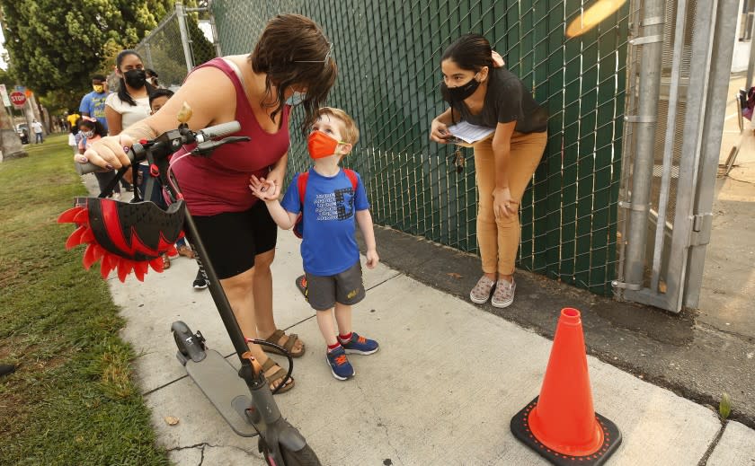 NORTH HOLLYWOOD, CA - AUGUST 17: Transitional Kindergartner Ryder White with mother Amber White checks in with Yazmin Magallon, Primary Promise Aide at Lankershim Elementary School in North Hollywood as parents and students check for the student name on a list using the Daily Pass website - designed to issue pre-approved health clearances for students to enter campus or present their QR code for entrance to the campus at Lankershim Elementary on Tuesday for the second day of in-class learning for LAUSD schools. "This is less chaotic today." Said Amber. The pre-approved health clearances for students to enter campus appeared to be up and working so the second day of school in the Los Angeles Unified School District appears to be going more smoothly than the first, largely devoid of the long lines and frustrations on back-to-school Monday when the district's student health-check system failed. Lankershim Elementary on Tuesday, Aug. 17, 2021 in North Hollywood, CA. (Al Seib / Los Angeles Times).