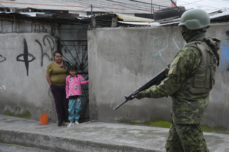 A soldier walks past residents on the south side of Quito, Ecuador, Friday, Jan. 12, 2024, in the wake of the apparent escape of a powerful gang leader from prison. President Daniel Noboa decreed Monday a national state of emergency, a measure that lets authorities suspend people’s rights and mobilize the military. (AP Photo/Dolores Ochoa)