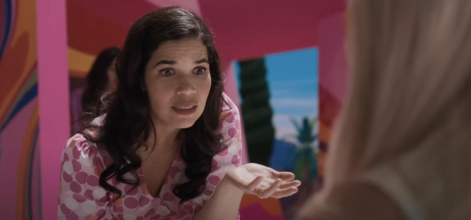 America Ferrera, in a scene from a "Barbie" looking at another character with a concerned expression, wearing a pink polka-dot blouse