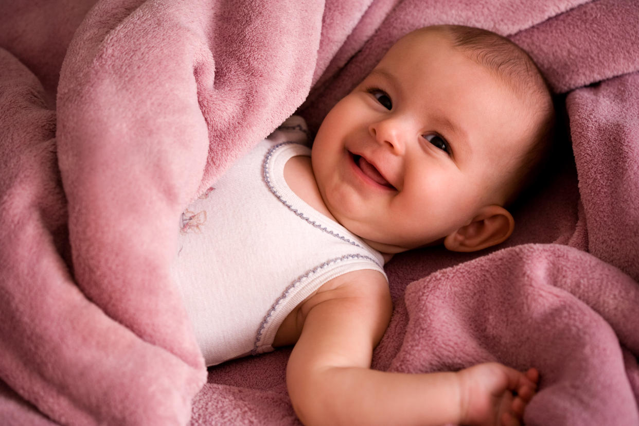  Smiling baby lying on pink blanket. 