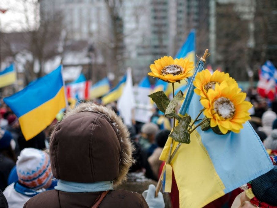 A person holds sunflowers and a Ukrainian flag at a rally in support of Ukraine