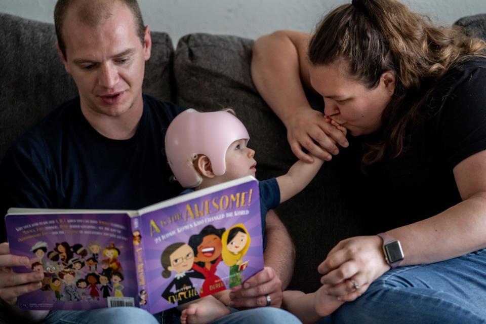 Madelynn Birchmeier reaches to have her hand kissed by her mother, Nicole, as her father, Adam, reads her a story in the living room of their home in Muskegon.