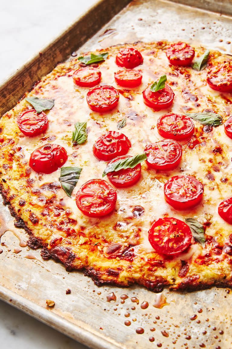 cauliflower crust pizza topped with cheese, tomato slices, and basil on a sheetpan