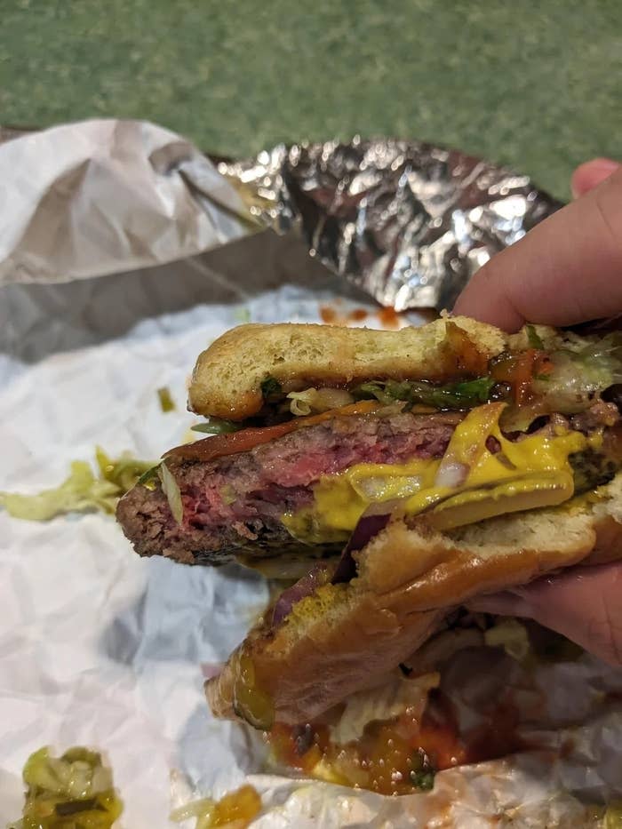 Close-up of a hand holding a partially eaten hamburger with lettuce and condiments