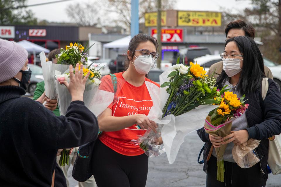 Roula AbiSamra, center, and Chelsey (last name withheld), right, prepare to lay flowers bouquets at a makeshift memorial outside of the Gold Spa in Atlanta, Wednesday, March 17, 2021.