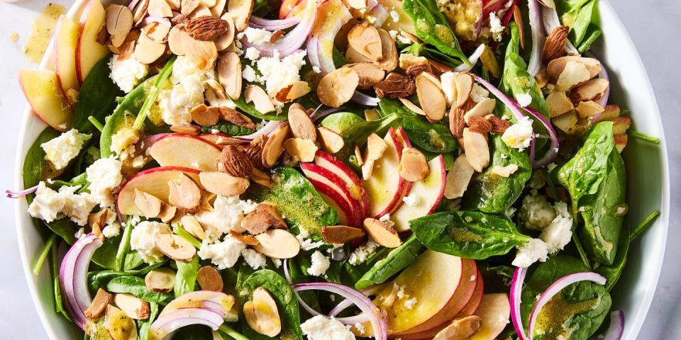 spinach in a bowl topped with sliced apples, sliced almonds, red onions, and crumbled feta