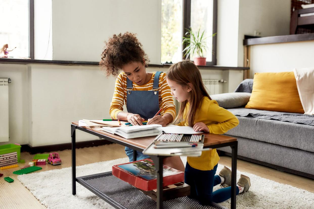 Caucasian little girl spending time with african american baby sitter. They are drawing, learning to write letters, sitting on the floor. Children education, leisure activities, babysitting concept