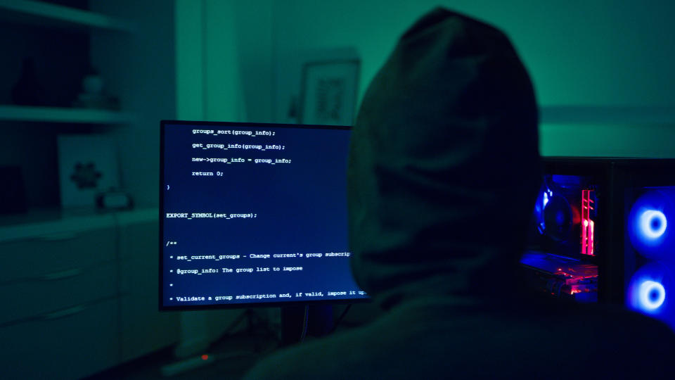 Hoodie, hacker and person at computer screen at night for cybersecurity, ransomware and fraud. Back of thief, spy hacking pc software for scam, phishing virus or crime of online firewall with malware