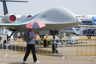 A man carrying an umbrella with the United States flag colors as he walks past the CH-6 drone during the 13th China International Aviation and Aerospace Exhibition, also known as Airshow China 2021 onTuesday, Sept. 28, 2021, in Zhuhai in southern China's Guangdong province. A state-owned Chinese aerospace company unveiled the military drone it says can stay aloft for up to 20 hours at altitudes as high as 15,000 meters (50,000 feet) at the opening Monday of the country's biggest air show.(AP Photo/Ng Han Guan)