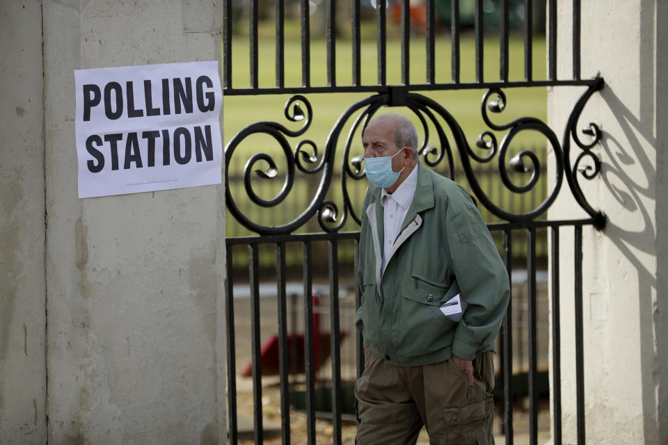 A men wearing a surgical mask to curb the spread of coronavirus walks past a sign for a polling station as he arrives to vote in London, Thursday, May 6, 2021. Millions of people across Britain will cast a ballot on Thursday, in local elections, the biggest set of votes since the 2019 general election. A Westminster special-election is also taking place in Hartlepool, England. (AP Photo/Matt Dunham)