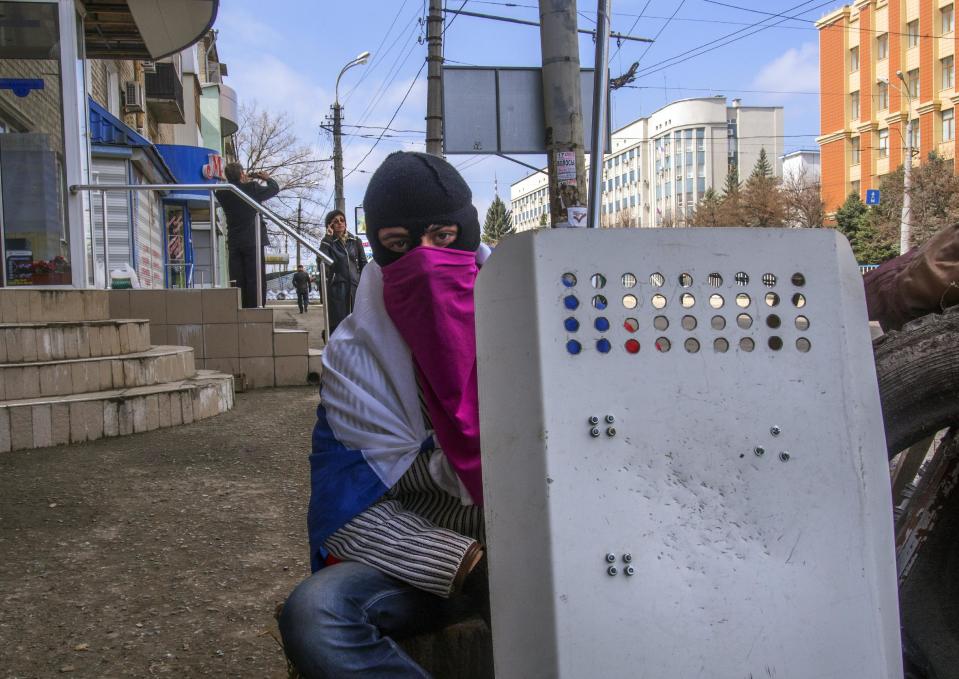 A masked pro-Russian activist looks at a photographer as he rests next to barricades at the Ukrainian regional office of the Security Service in Luhansk, 30 kilometers (20 miles) west of the Russian border, in Ukraine, Wednesday, April 9, 2014. Ukrainian Interior Minister Arsen Avakov said the standoff in Luhansk and the two neighboring Russian-leaning regions of Donetsk and Kharkiv must be resolved within two days. (AP Photo/Igor Golovniov)