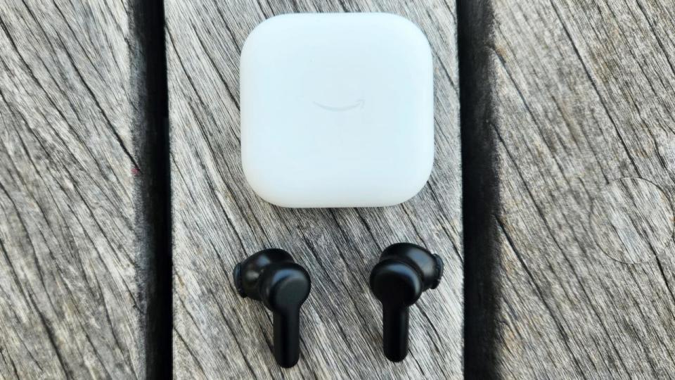 The Amazon echo buds are arranged on a gray wood deck. 