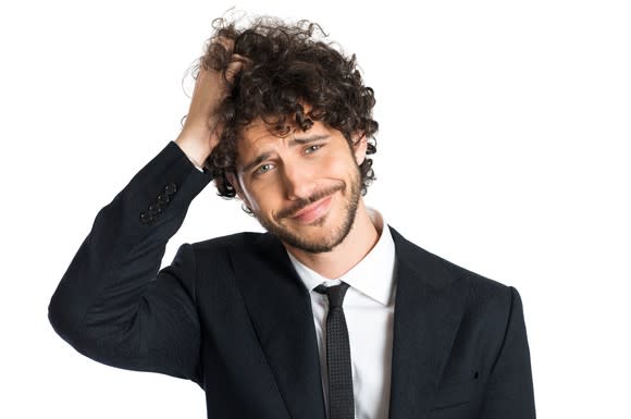 A confused young man in a suit scratching the top of his head.