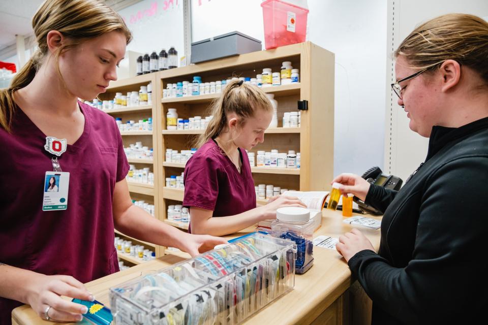 Pharmacy tech students Brianna Burdett, left, of Claymont High School, and McKenzie Stubbins of Dover High School practice dispensing pills, while Liberty Humerickhouse of Dover High School the role of a customer, at Buckeye Career Center in New Philadelphia.