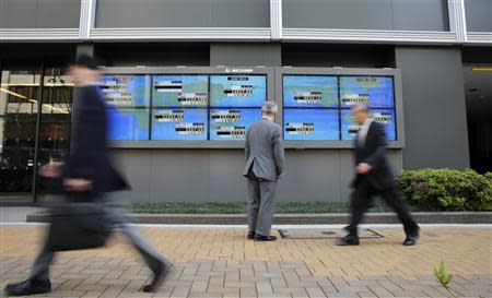 A man looks at an electronic board displaying Japan's Nikkei average (top C) and various countries' stock indices, as passers-by walk past outside a brokerage in Tokyo April 16, 2014. REUTERS/Toru Hanai