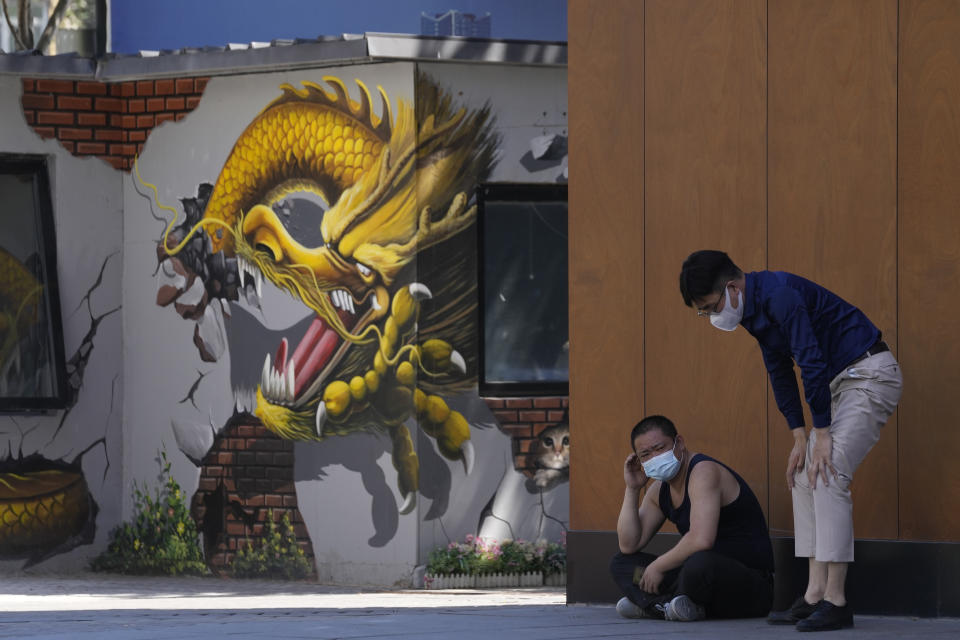 Residents wearing masks rest in the shade near a graffiti of a dragon, Friday, May 27, 2022, in Beijing. (AP Photo/Ng Han Guan)