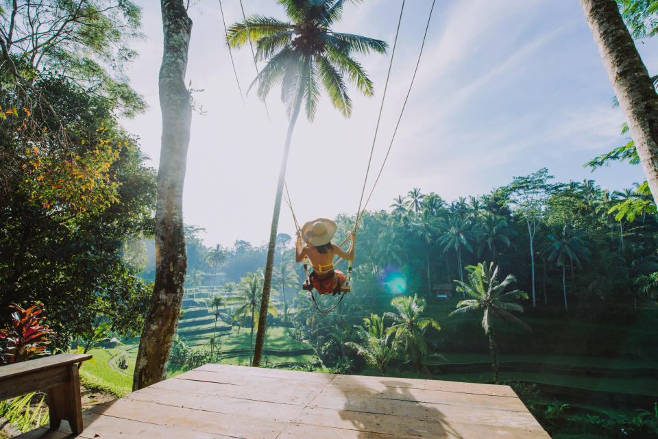 Woman using a swing over the jungle and Bali rice fields in Tegalalang, Ubud