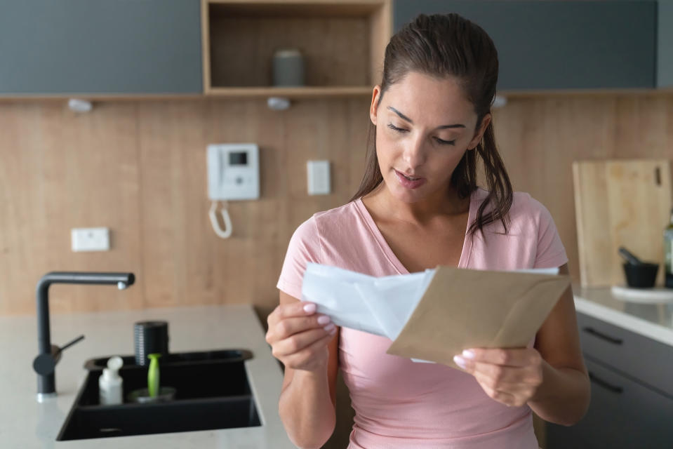 Portrait of a beautiful woman at home checking her mail in the kitchen holding envelopes - lifestyle concepts