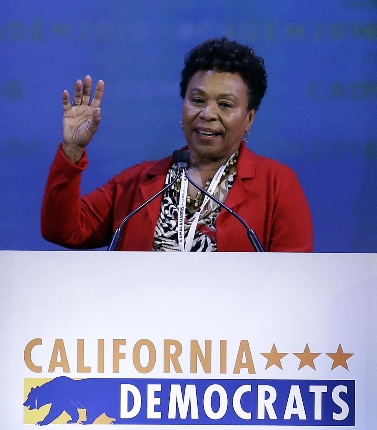 Rep. Barbara Lee waves as she speaks at the microphone above a banner that says California Democrats and shows the state's symbol, a grizzly bear.