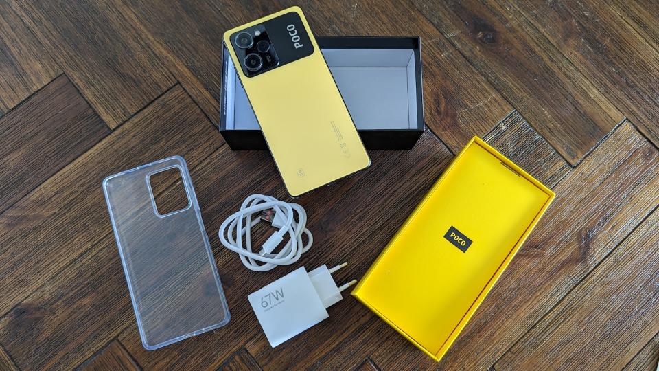 A yellow POCO X5 Pro phone with the contents of its packaging on a wooden table.