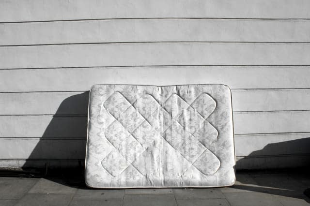 Old mattress leaning up against wall on street.