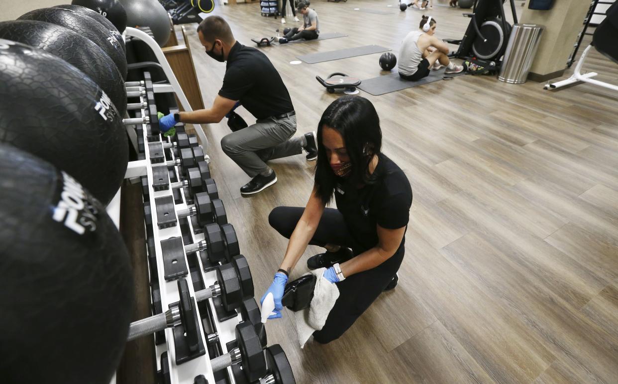 Jason Nichols, left, facilities operation manager at Life Time, and Jennifer McKeon, right, facilities operations national manager at Life Time, disinfect hand weights at the Life Time Biltmore as it opens for business after being closed due to the coronavirus on Monday, May 18, 2020, in Phoenix, Ariz.