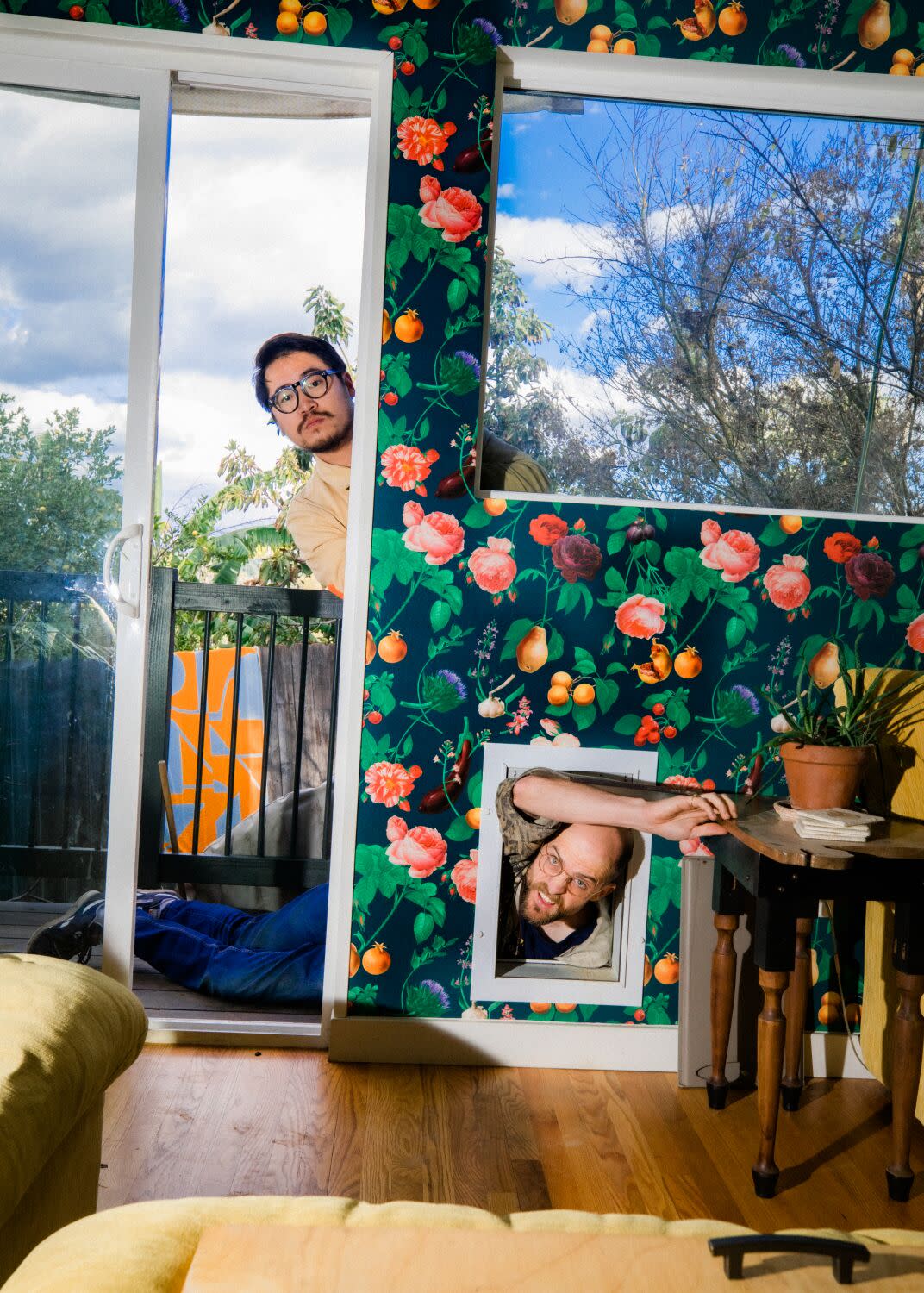 One man peers through a screen door into a house while another pretends to climb through the doggie door for a portrait.