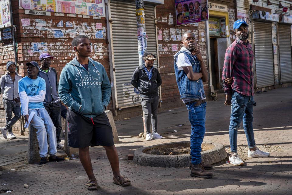Young men watch residents lining up to be tested for COVID-19 as well as HIV and Tuberculosis, in downtown Johannesburg Thursday, April 30, 2020. Thousands are being tested in an effort to derail the spread of coronavirus. South Africa will began a phased easing of its strict lockdown measures on May 1, although its confirmed cases of coronavirus continue to increase. (AP Photo/Jerome Delay)