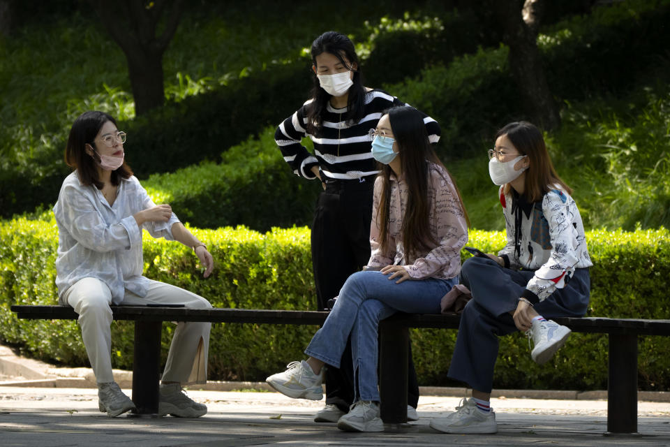 People wearing face masks talk as they sit on benches at a public park in Beijing, Tuesday, Aug. 30, 2022. (AP Photo/Mark Schiefelbein)