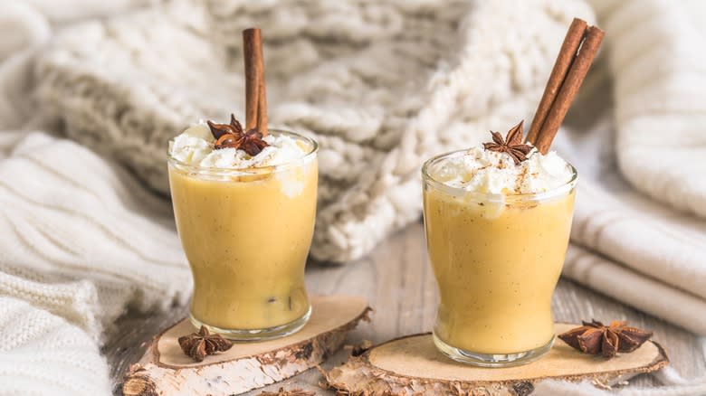 Two Coquito drinks with cinnamon sticks