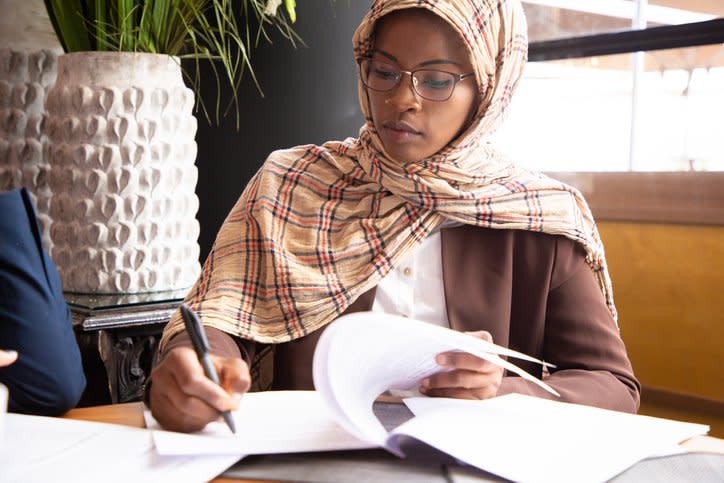 A woman sits at a table in a conference room and signs documents.