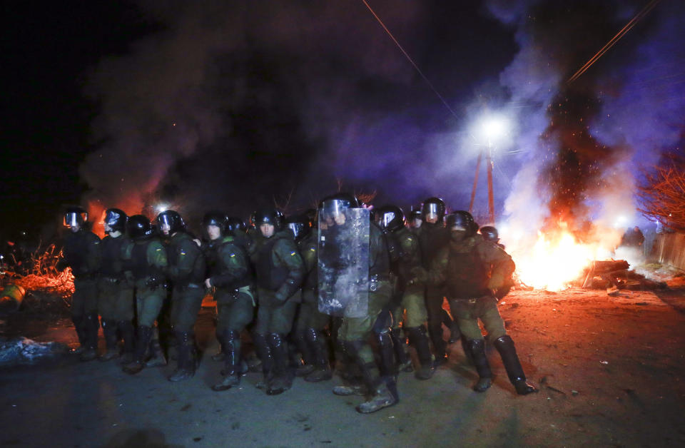 Ukrainian riot police prepare to push back protesters, who planned to stop buses carrying passengers evacuated from the Chinese city of Wuhan, outside Novi Sarzhany, Ukraine, Thursday, Feb. 20, 2020. Several hundred residents in Ukraine's Poltava region protested to stop officials from quarantining the evacuees in their village because they feared becoming infected. Demonstrators put up road blocks and burned tires, while Ukrainian media reported that there were clashes with police, and more than 10 people were detained. (AP Photo/Efrem Lukatsky)