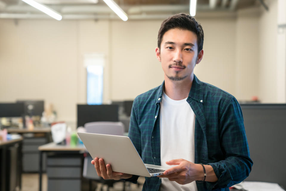 Young asian man holding a laptop against office backdrop, illustrating a story on a LinkedIn study on new jobs among Singapore workers.