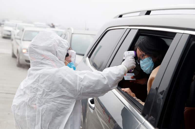 A medical worker in protective suit checks the body temperature of a car passenger at a checkpoint outside the city of Yueyang