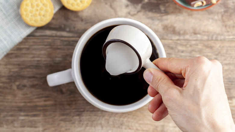 Person adding creamer to coffee