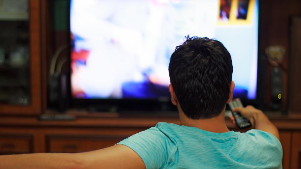 Male watching television in home living room / channel hopping.