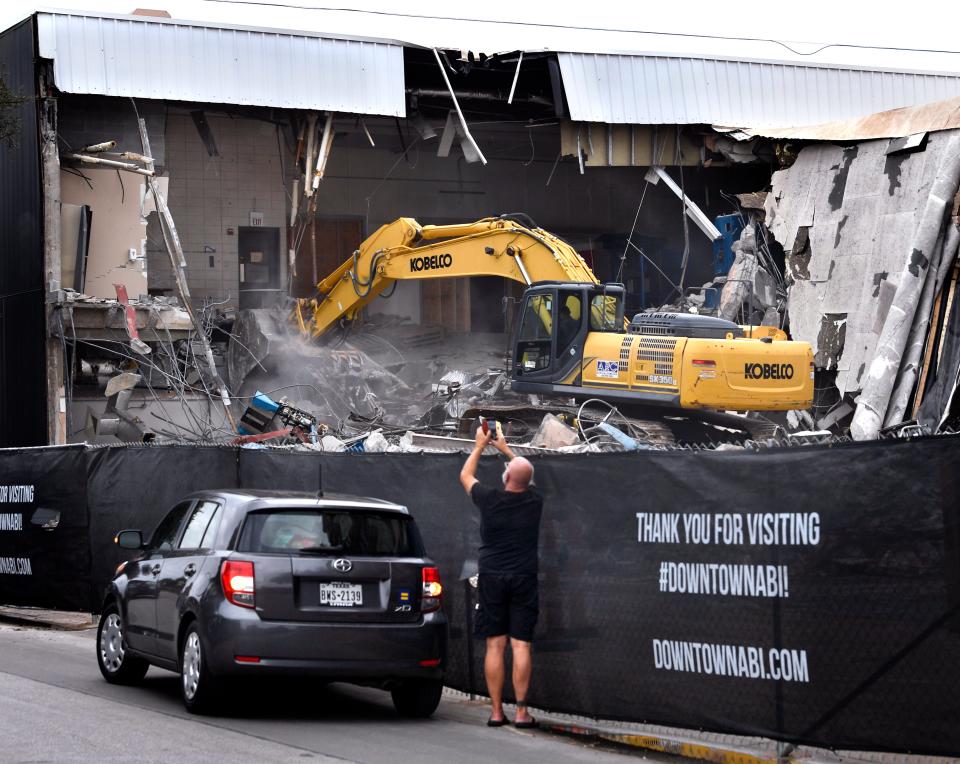 A passerby photographs an excavator digging into the former Abilene Reporter-News building Oct. 17. It was the first day of demolition for the structure.