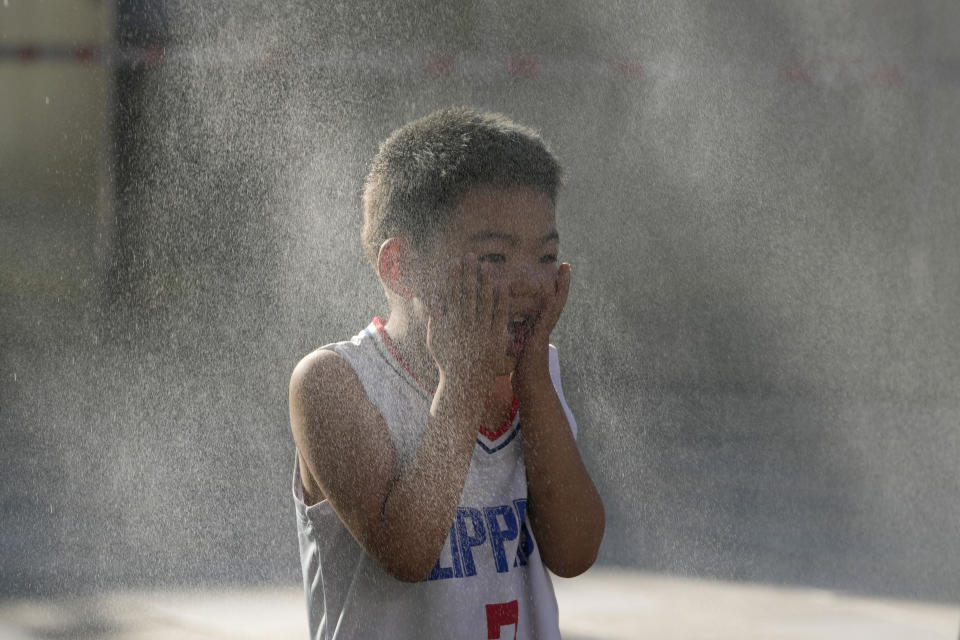 A child reacts to a mist machine as he cools off from the summer heat in Beijing, Saturday, June 15, 2024. (AP Photo/Ng Han Guan)