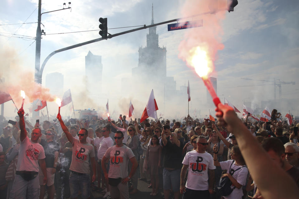 People stand on the city's main intersection holding national flags and flares to observe a minute of silence for the fighters and victims of the 1944 Warsaw Uprising against the Nazi German occupiers, in Warsaw, Poland, Monday Aug. 1, 2022. Poles are marking the 78th anniversary of the Warsaw Uprising, a doomed revolt against Nazi German forces during World War II. (AP Photo/Michal Dyjuk)