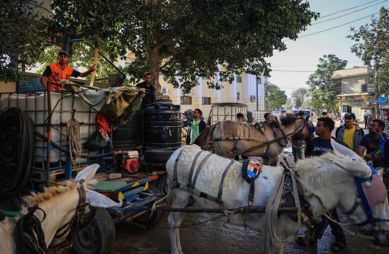 Palestinos se reúnen junto a carros tirados por burros cargados con tanques de agua para la venta, en Khan Yunis, en el sur de la Franja de Gaza, el 30 de octubre de 2023.