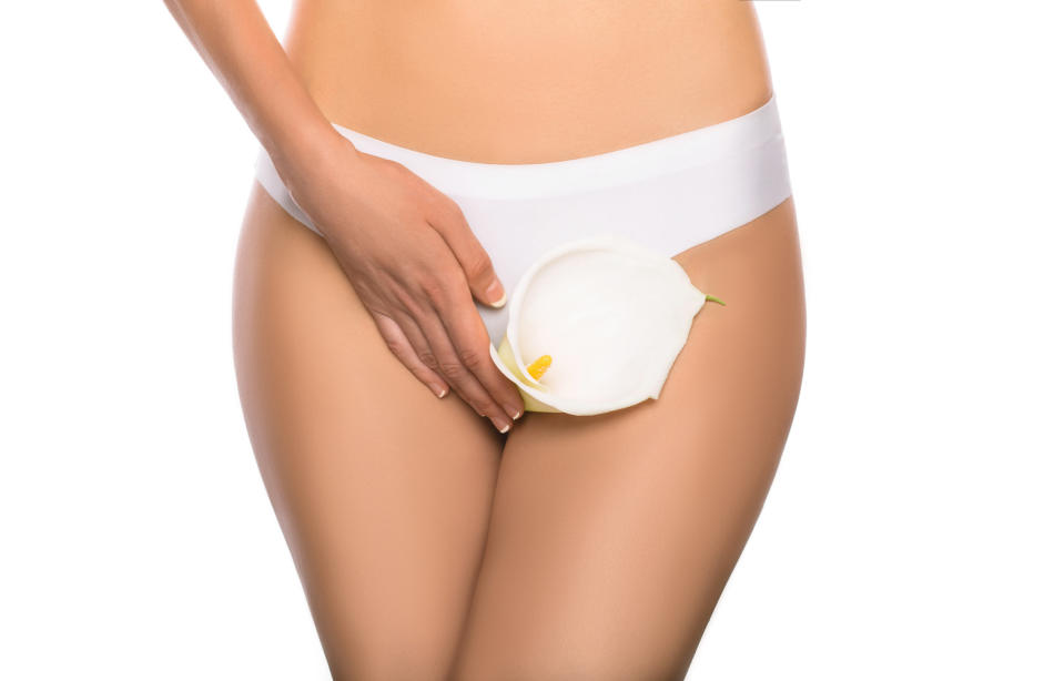 A person wearing white underwear holds a white calla lily flower in front of their pelvic area