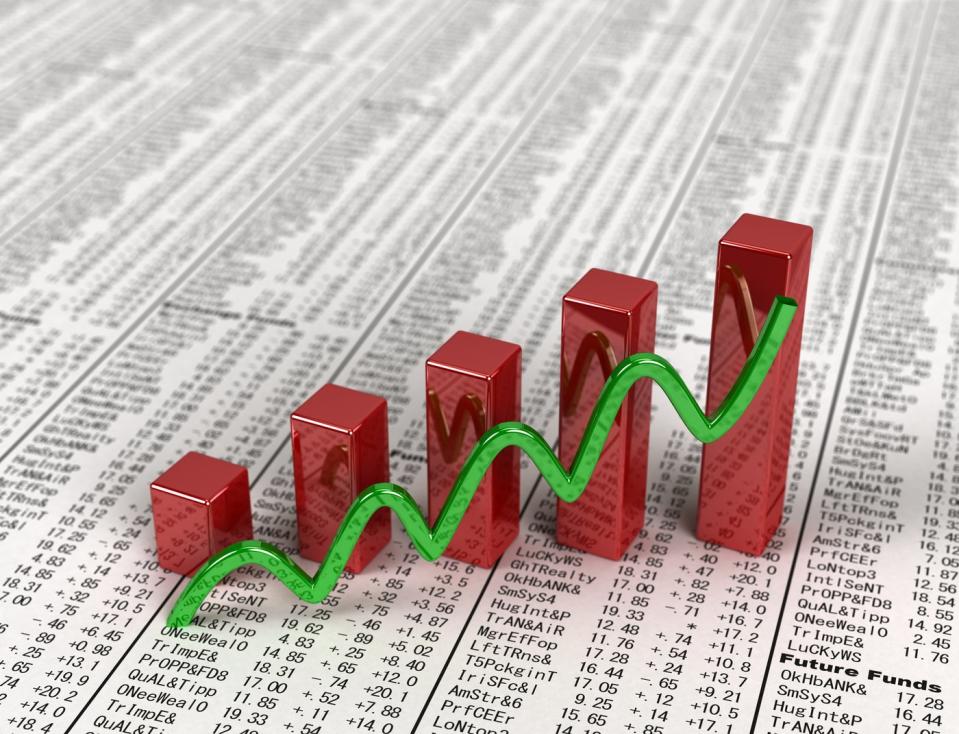 A rising wavy green line and ascending red bar chart set atop a financial newspaper with visible stock quotes.