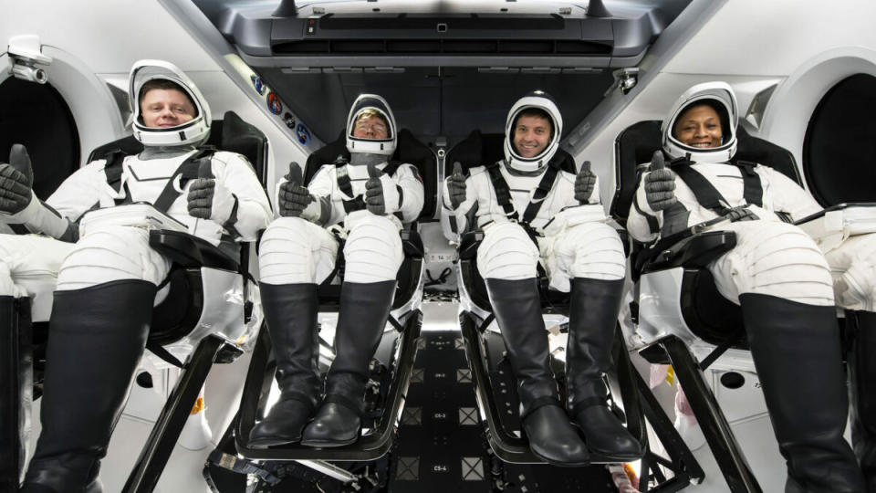 Four astronauts dressed in white launch spacesuits make a thumbs up sign.