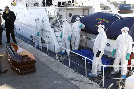 Health workers stand near a coffin with the dead body of a migrant, which was carried off a navy ship at the Sicilian harbour of Empedocle December 5, 2014. REUTERS/Antonio Parrinello